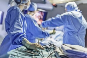 a group of medical professionals, likely surgeons, in an operating room. They are performing a surgical procedure and wearing standard attire, including gloves, caps, and surgical gowns.