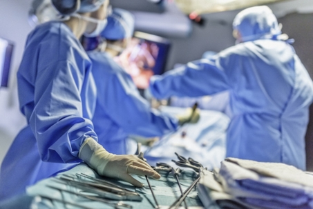 a group of medical professionals, likely surgeons, in an operating room. They are performing a surgical procedure and wearing standard attire, including gloves, caps, and surgical gowns.