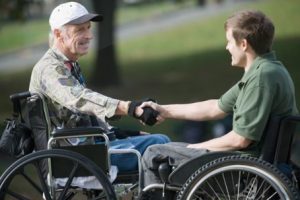 Two individuals in wheelchairs shake hands outdoors, symbolizing friendship, support, and inclusivity.