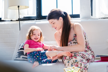 The action in the image shows an adult tending to a child's leg while seated on a white couch in a well-lit room.