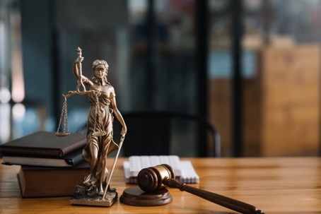 A desk featuring symbols of justice: a Lady Justice statue, law books, a gavel, and note cards, evoking a legal and courtroom setting.