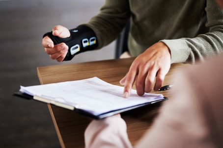 Two individuals at a table discussing a document, with one wearing a wrist brace and holding a pen