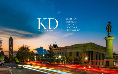 The image displays the logo for a law firm named KD Trial Lawyers, set against an urban cityscape at dusk.