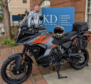 A motorcycle is parked on a brick pathway in front of a sign that displays "KD Trial Lawyers" alongside names such as Killoren, Kissinger, Dantin, Denton & Dunham, PC.