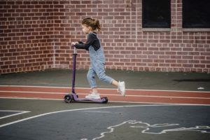 a child riding a purple scooter outdoors on a marked court