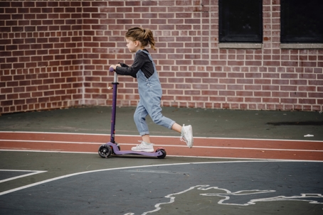 a child riding a purple scooter outdoors on a marked court