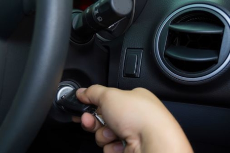 A hand grips a key, turning it in the ignition of a car.