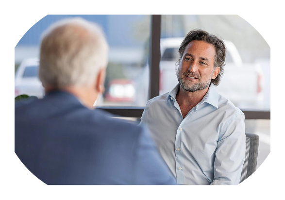 Two men in a modern office setting, one smiling in a light blue shirt, engaged in conversation.